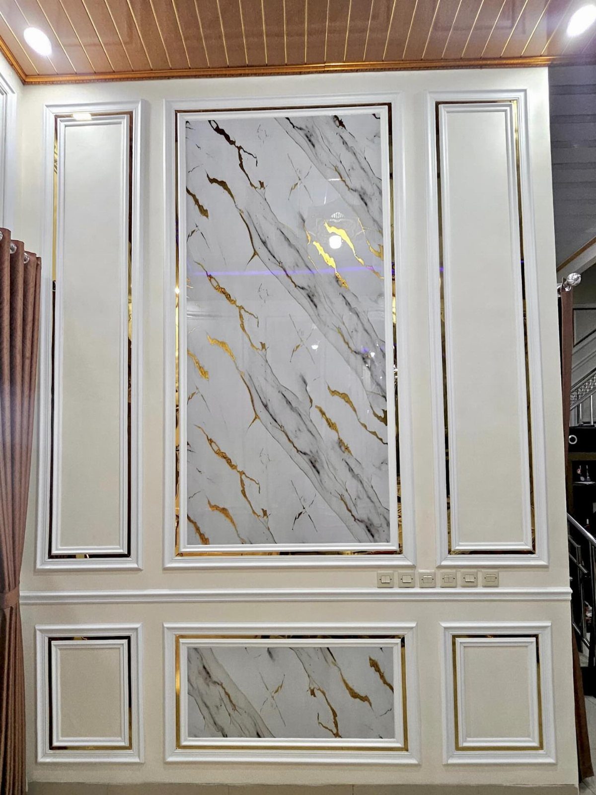 8 Wall Molding Design Ideas for Rooms That Need More Structure 7 White wall panels with gold trim and marble-patterned inserts in a decorated room.