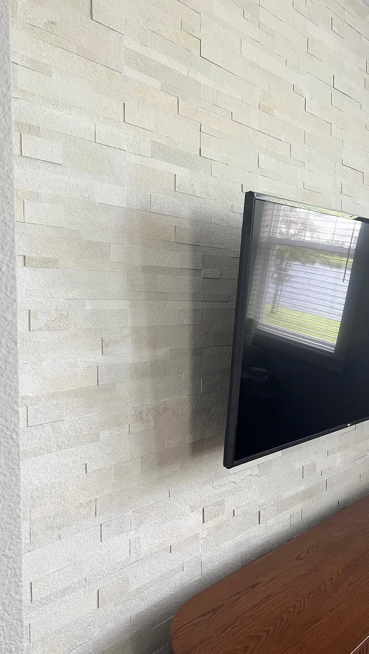 Textured light stone wall panels with a black television mounted on the surface.