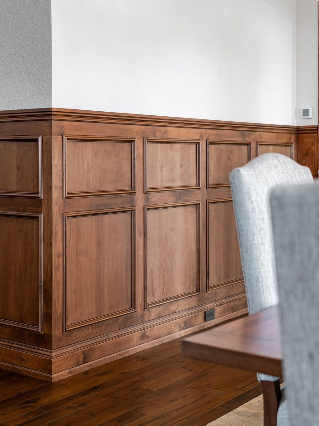 Wooden wainscoting with raised rectangular panels installed on the lower half of a white wall.