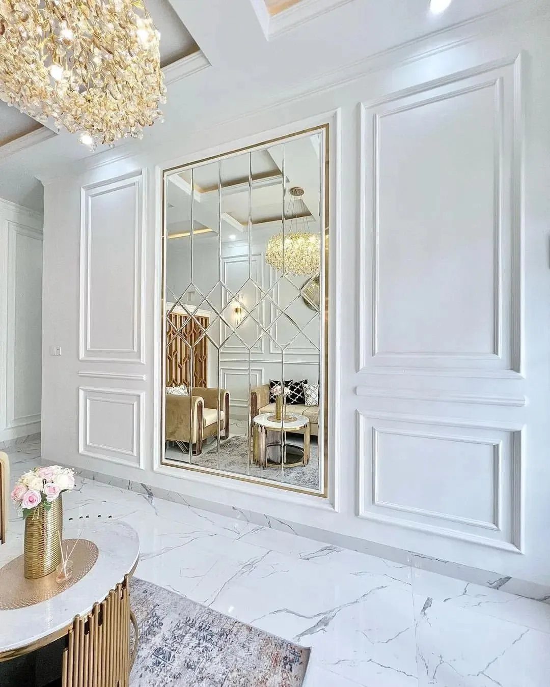 White wall panel molding with raised rectangular panels surrounding a large gold-framed mirror.