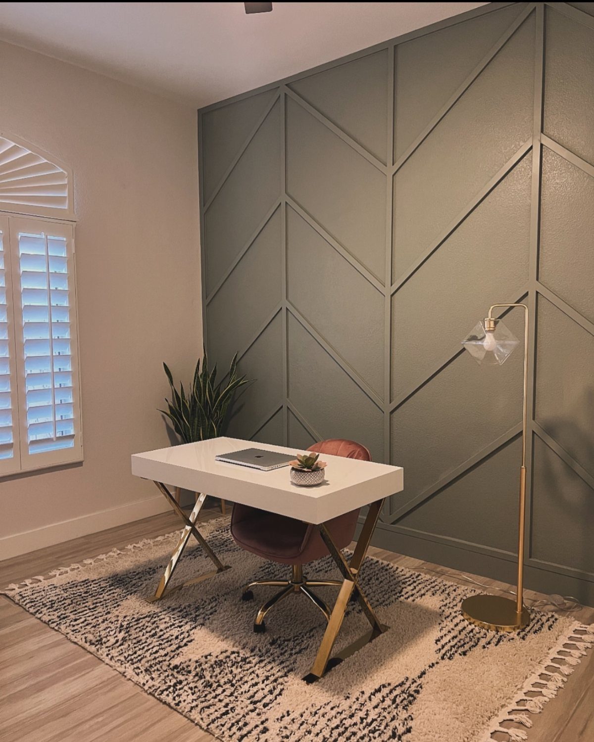 A sage green wall with a geometric chevron pattern behind a white desk and chair.