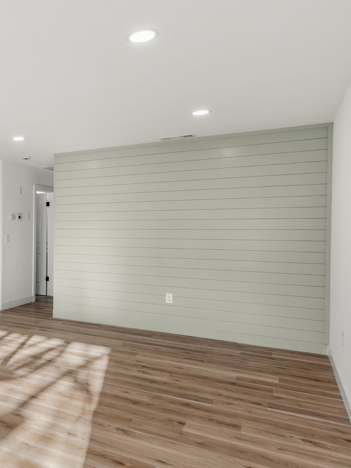 Horizontal sage green shiplap planks covering a large interior accent wall.
