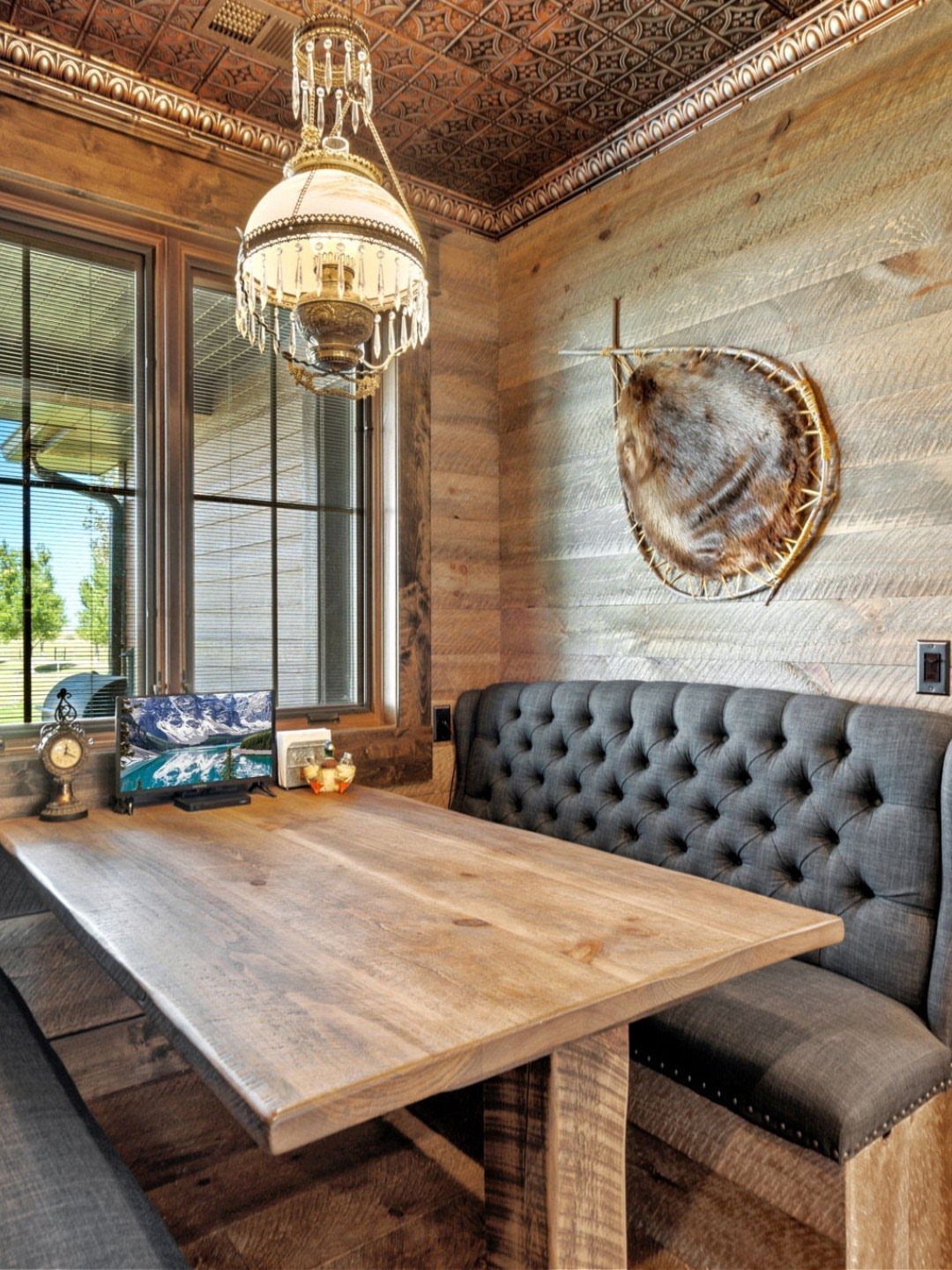 Wooden dining nook with a tufted grey banquette, wooden table, and light wood plank walls.