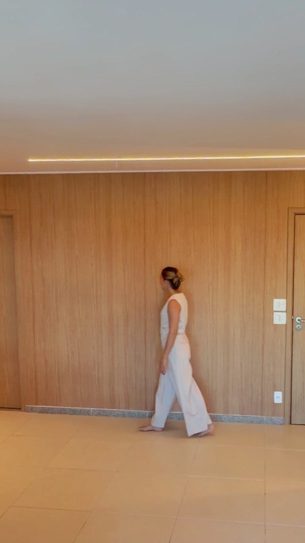 A woman walking across a room in front of a large wood paneled wall.
