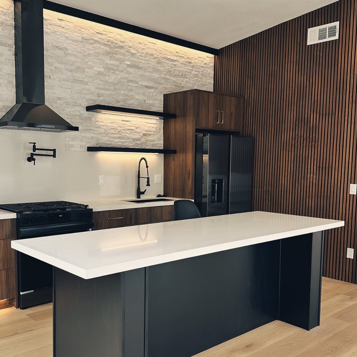 Modern kitchen with black appliances, white countertops, and a dark wood slatted accent wall.