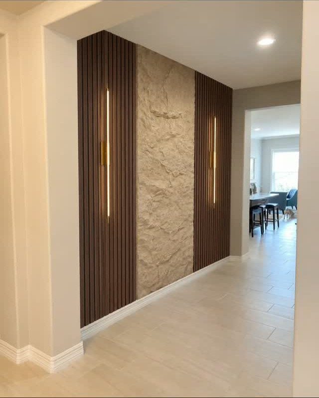Vertical wood slats with integrated lighting flanking a textured stone wall panel in a hallway.