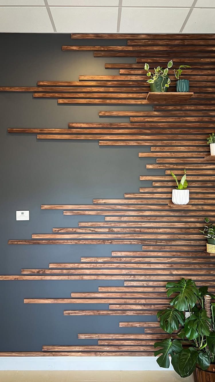 Staggered dark wood planks arranged in a geometric pattern on a grey accent wall with plants.