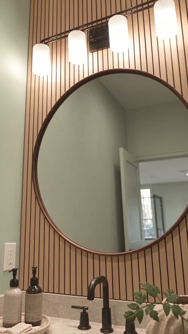 Vertical light wood slats covering a bathroom wall behind a large round mirror.