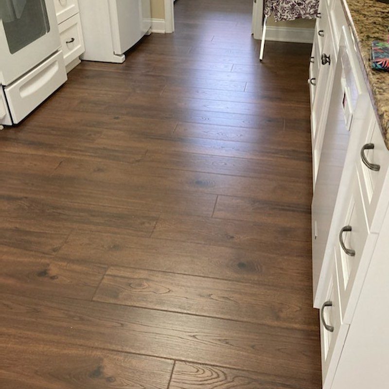 Dark brown wooden floor planks installed in a kitchen between white cabinetry.